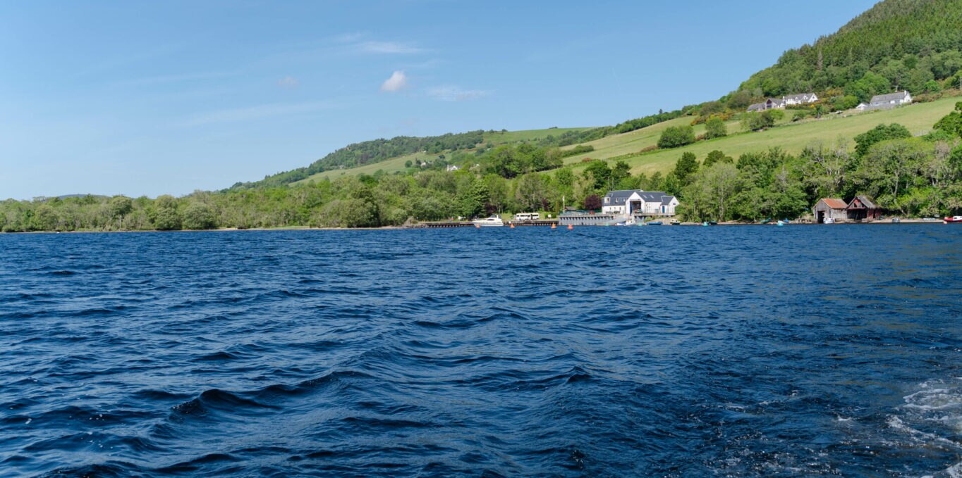 A large loch of water with green rolling hills in the background. 
