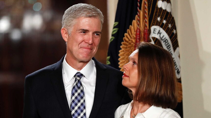 Neil smiling next to his wife, who is looking up at him, a flag draped in the background.