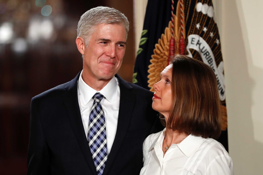 Neil smiling next to his wife, who is looking up at him, a flag draped in the background.