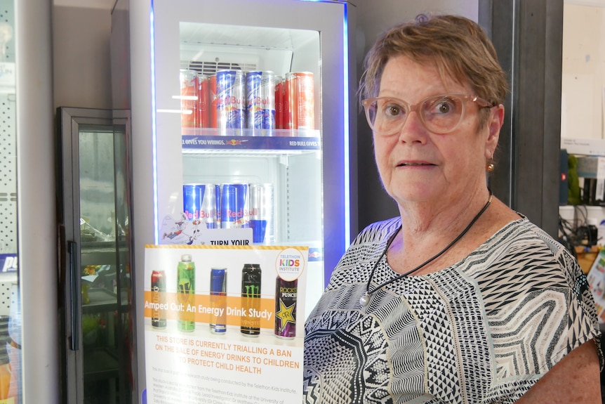 A woman stands in a shop in front of a half empty fridge.