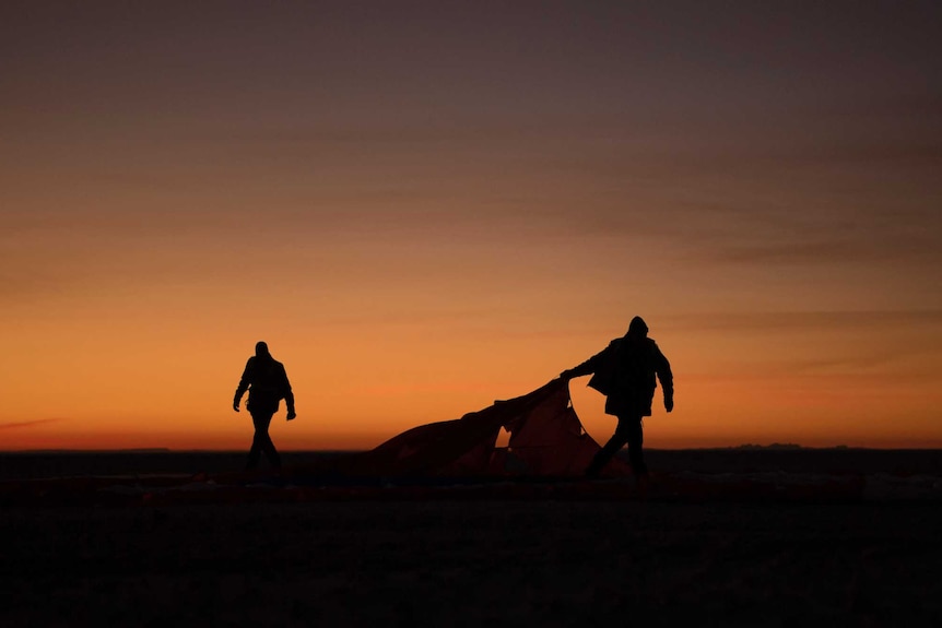 Boeing, NASA, and U.S. Army personnel collect parachutes in front of a glowing orange sky.