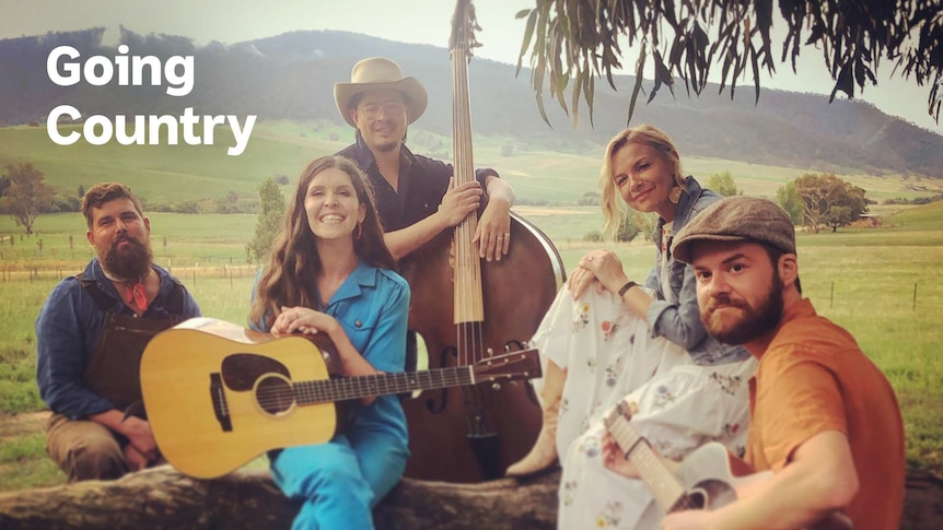 Justine Clarke sits amongst friends against an Australian country backdrop with hillsides and pasture
