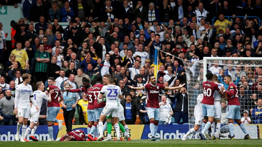 Leeds United (white shirts) and Aston Villa (claret) players fight in front of a grandstand full of celebrating supporters