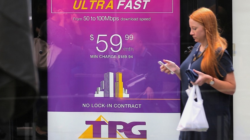 A woman looks at her phone as she walks past an advertisement for Australia's TPG Telecom Ltd in central Sydney.