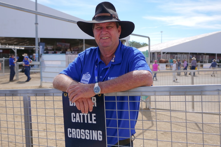 Gordon Ryan, blue shirt, dark hat, smiles leaning on gate that says "danger cattle crossing".