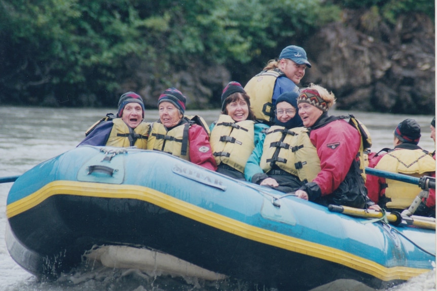 A large inflatable boat sails on a bustling river. On it is a group of people laughing, among them Yvonne Kennedy, smiling.