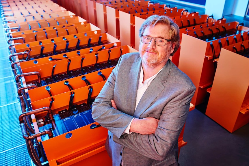 Matt Lamont standing beside a huge, orange supercomputer, with his arms crossed