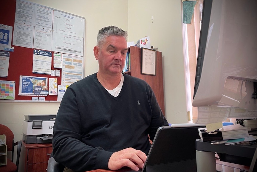 Un homme en pull noir regarde un écran d'ordinateur, dans un bureau.