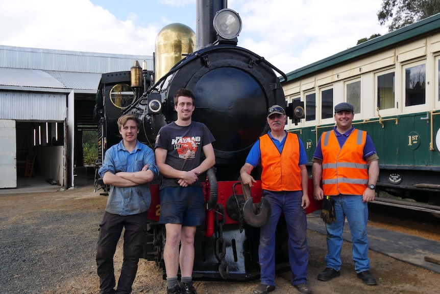 A group of four men stand in front of an old steam locomotive. 