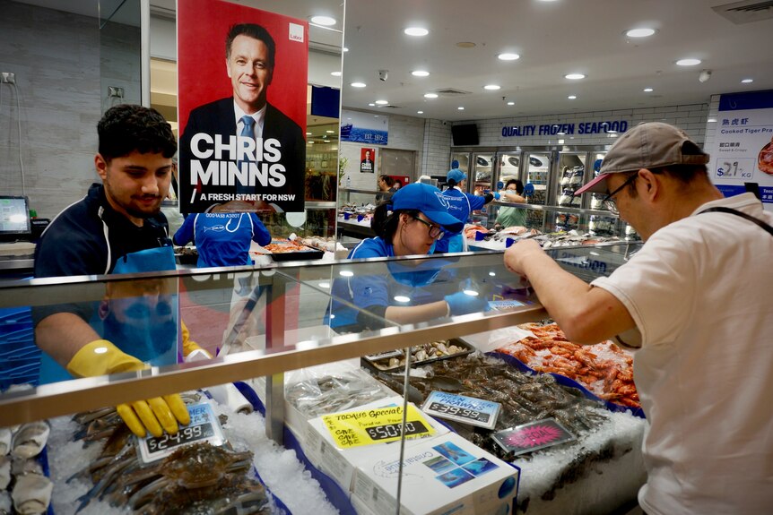Man and woman serve seafood to a customer, with Chris Minns poster behind them