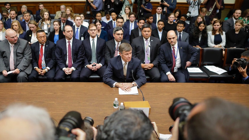 Joseph Maguire sits down in front of a pack of photographers and in front of suited men at House Intelligence Committee