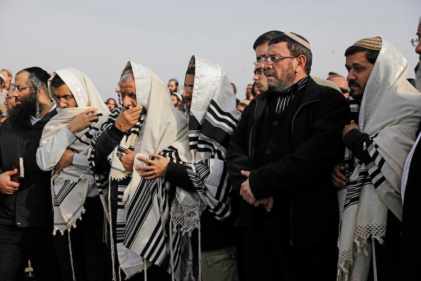 Men and women are seen mourning while dressed in traditional Israeli dress.