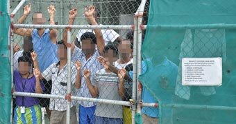 Asylum seekers stare at media from behind a fence