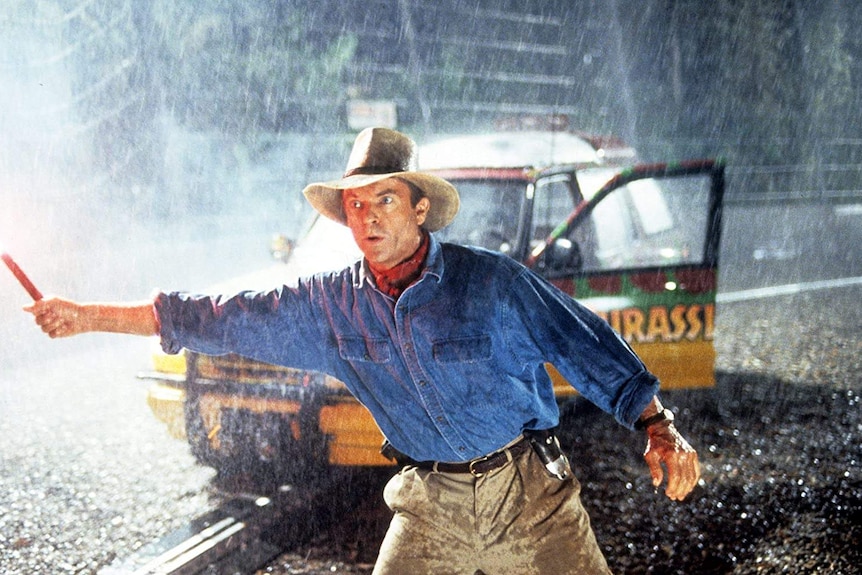 A still from the 90s film Jurassic Park showing actor Sam Neill holding a flare in the rain