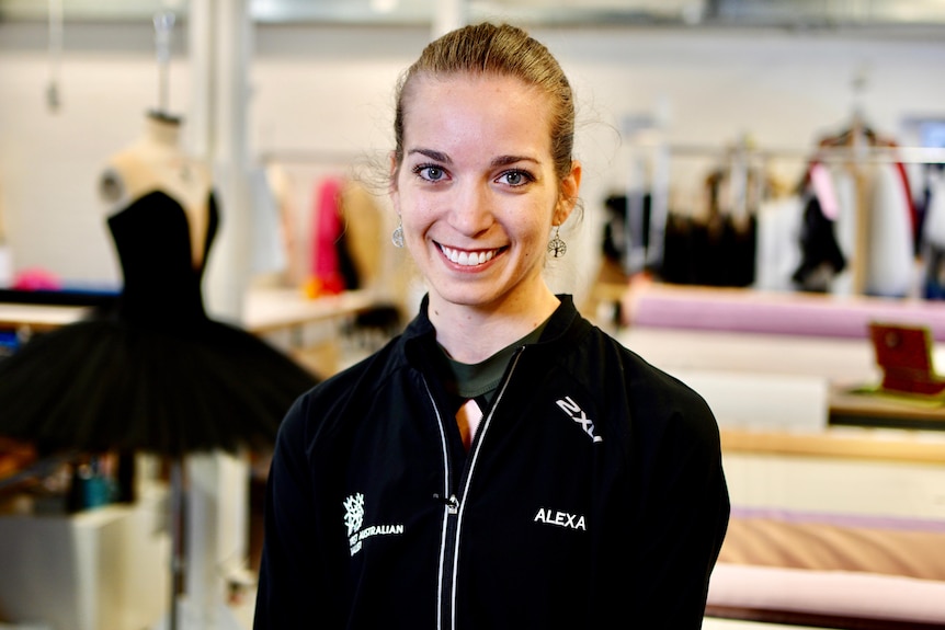 A head and shoulder shot of Alexa Tuzil smiling and being photographed in front of stage costumes