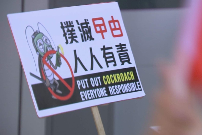 A close up of a sign in a crowd which shows an illustration of an anthropomorphic cockroach holding a molotov cocktail.