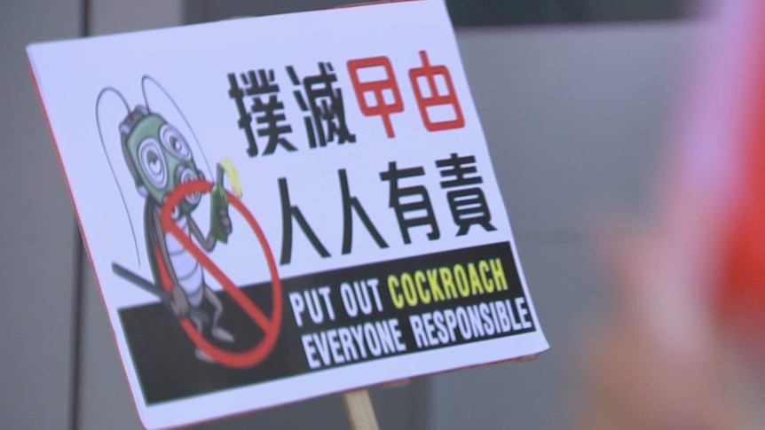 A close up of a sign in a crowd which shows an illustration of an anthropomorphic cockroach holding a molotov cocktail.