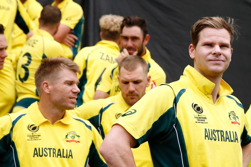 Steve Smith and the Australian cricket team stand on the boundary during a rain delay.