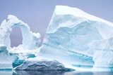 A whitish-blue iceberg floating in grey water.