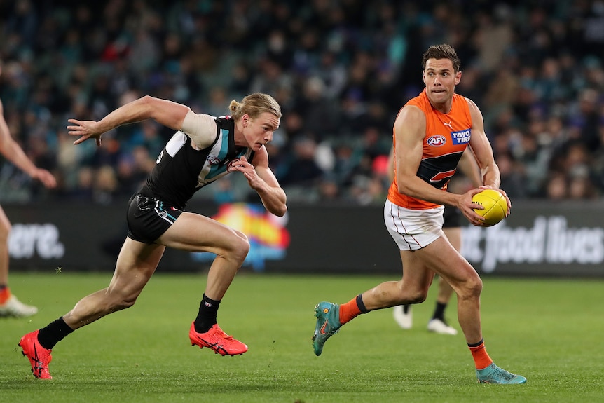 A GWS player looks up as he runs with the ball as a Port Adelaide defender puts his head down to chase behind him.