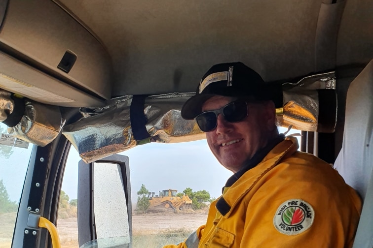 A smiling man in a firefighter's uniform sits in the cabin of a truck.