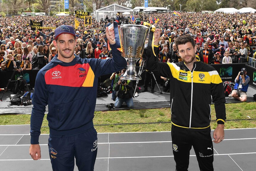 Taylor Walker and Trent Cotchin smile while holding the premiership cup in front a crowd of fans.