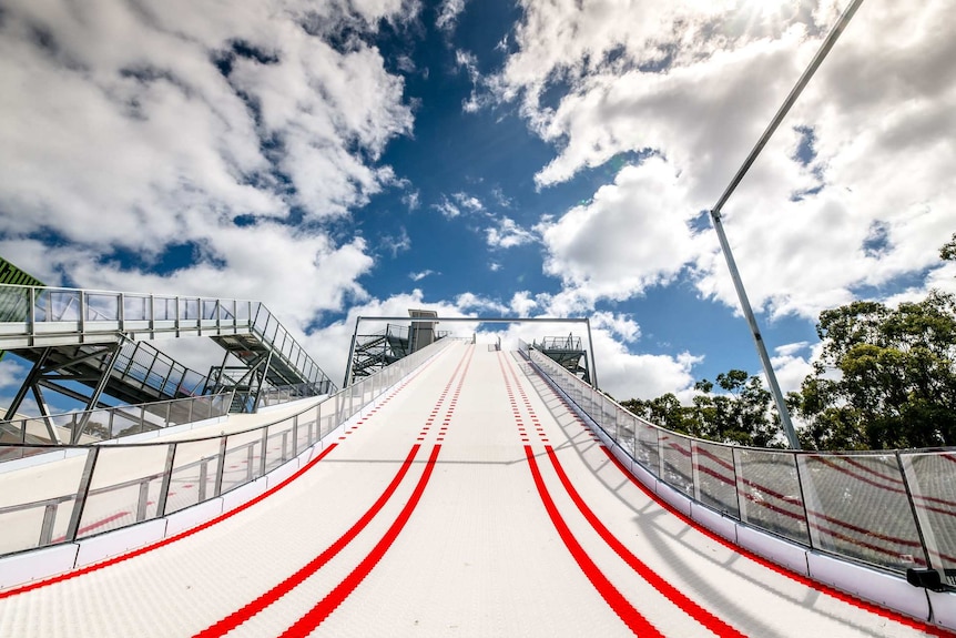 A low view looking up of a steep white and red track with clouds and blue sky in the distance.