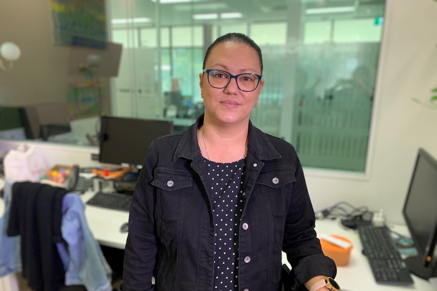 Woman in dark shirt with her hair tied back looks at camera