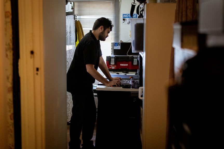 A man working in a computer in a cramped workshop full of tools and electronics.