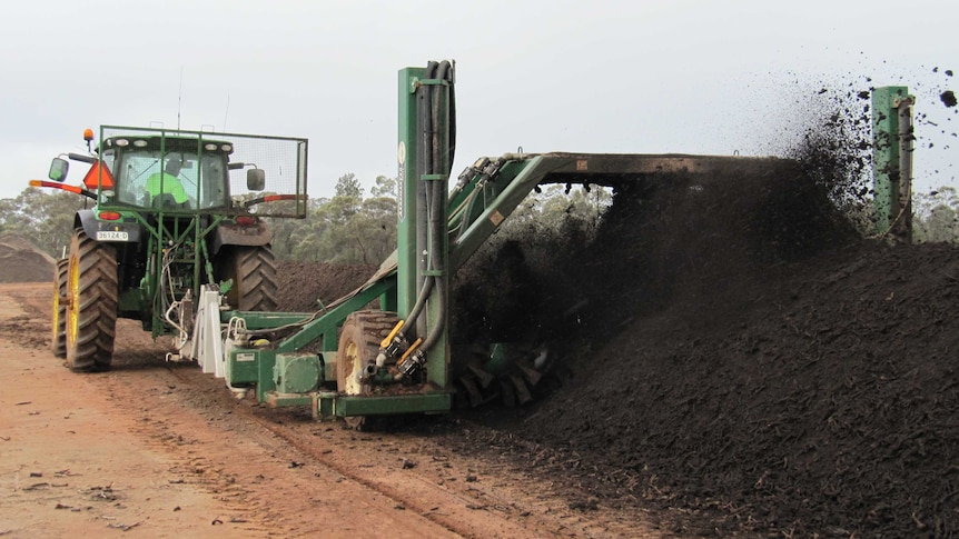 A tractor with a mechanical turner travels through a long row of compost