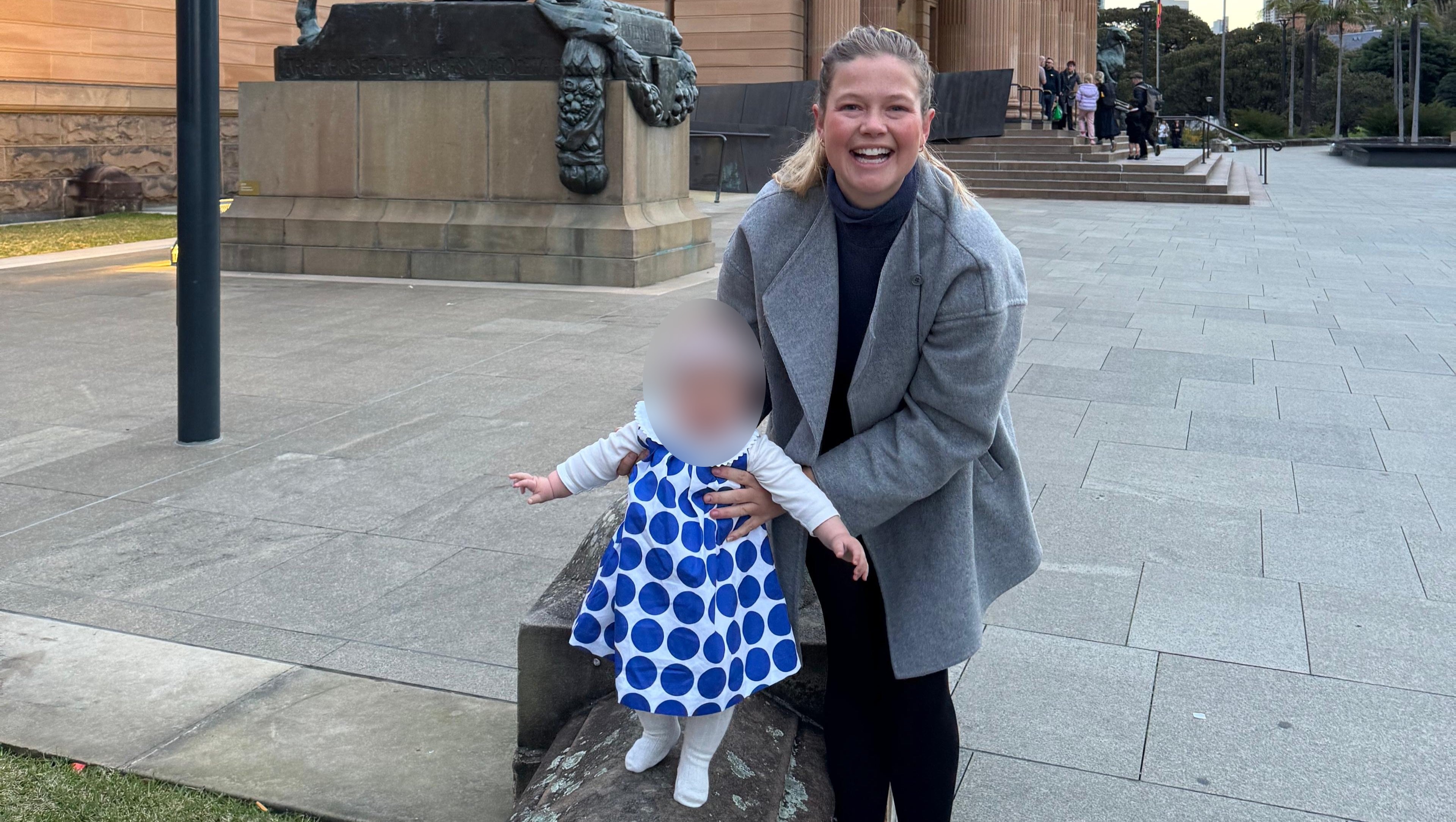 leah stewart smiles at the camera while holding the hands of her baby daughter outdoors
