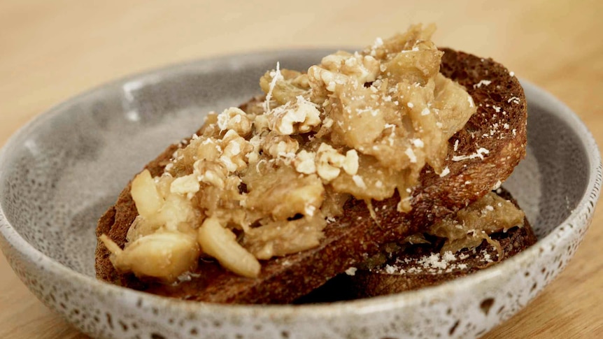 Braised fennel on rye toast with crushed walnuts and Padano cheese, two slices sit in a blue bowl on a kitchen bench.