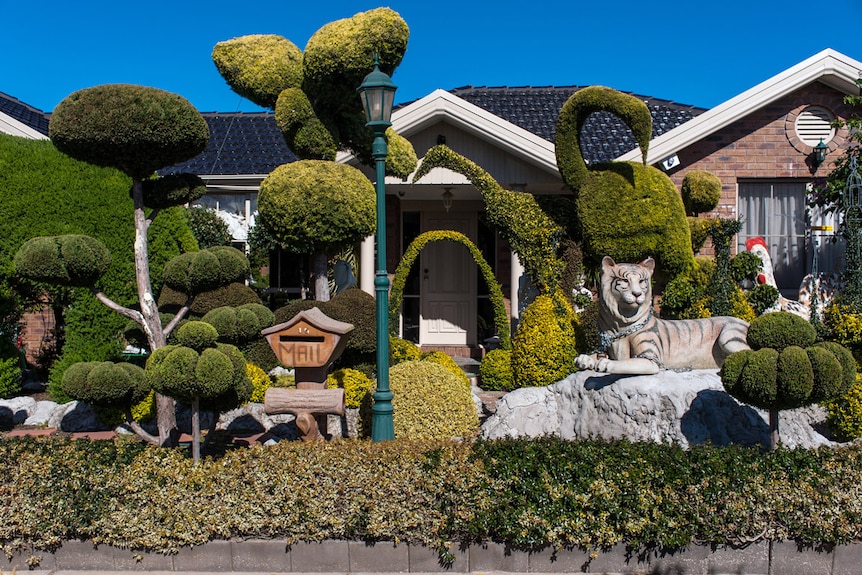 A brick suburban house, photographed from the street, featuring topiary and a concrete tiger.