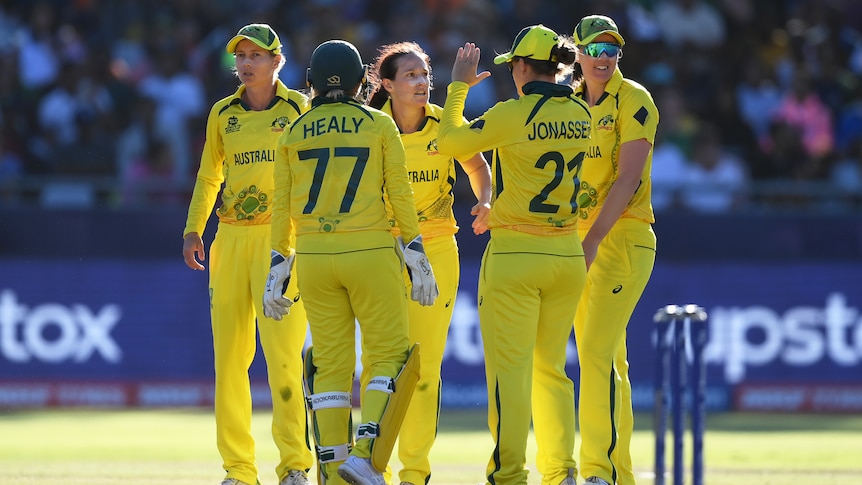 An Australian fast bowler stares intently as her teammates congratulate her for a wicket in the T20 World Cup final,