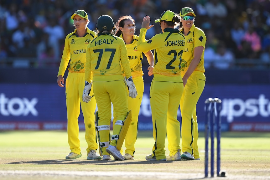 An Australian fast bowler stares intently as her teammates congratulate her for a wicket in the T20 World Cup final,