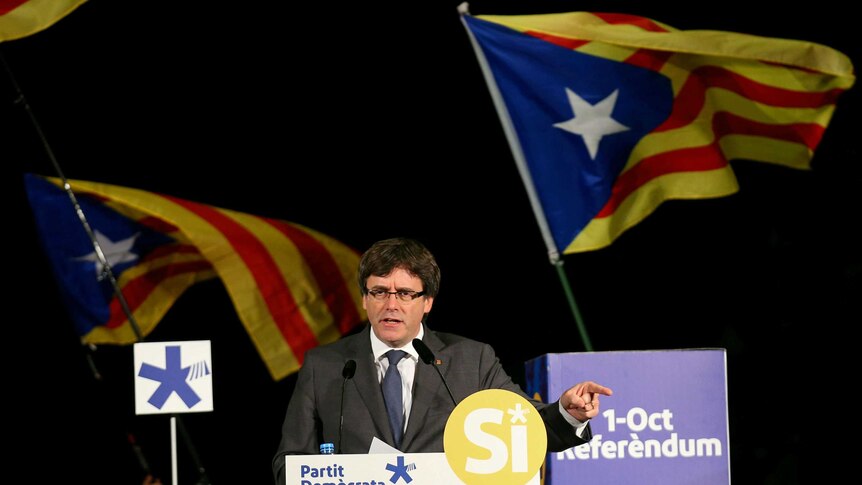 Former Catalan president Carles Puigdemont gestures behind a lectern.