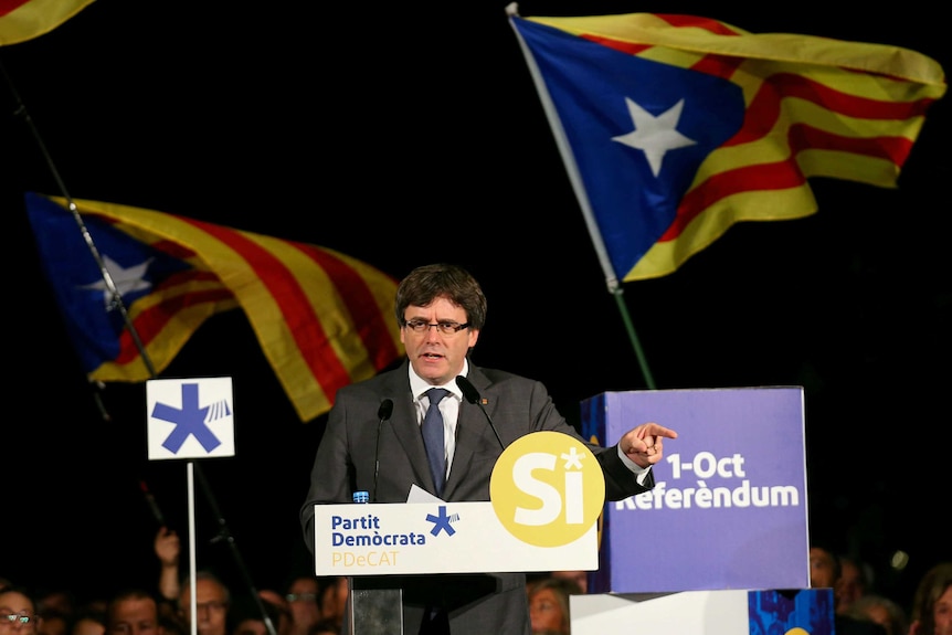 Former Catalan president Carles Puigdemont gestures behind a lectern.