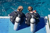Two scuba divers sit ready to enter the water off Cairns