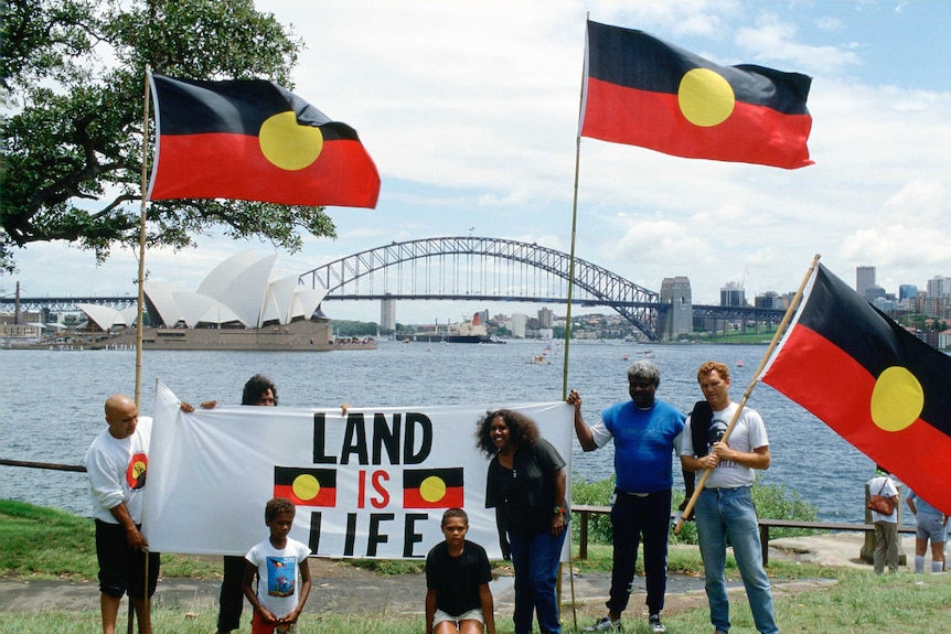 Indigenous Australians hold flags and a sign saying "Land is for Life" during a protest in Sydney.