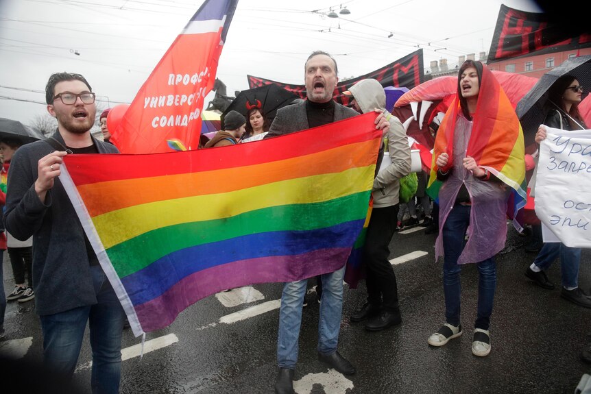 two men holding a rainbow flag among a crowd carrying flags and banners