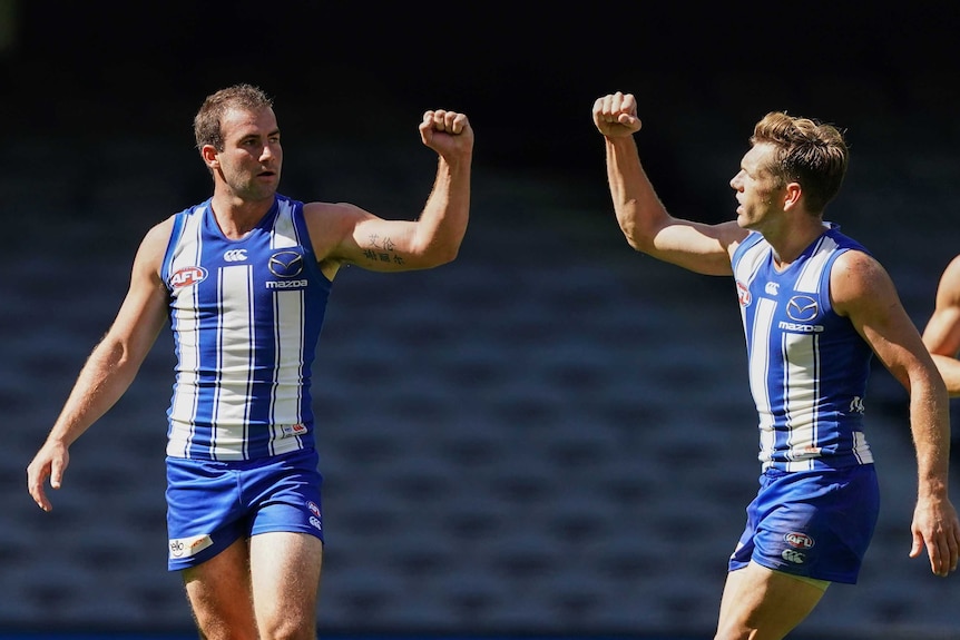 Two AFL teammates pump their fists while keeping their distance after a goal for their team.