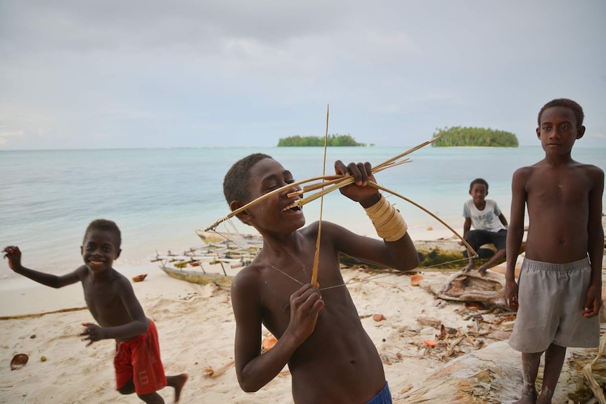 A smiling boy holds up a small toy bow and arrow with other boys in the background.