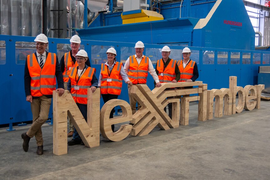 A group of people pose for a photo next to a NeXTimber sign.