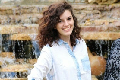 A young woman smiles as she poses for a photograph in front of a fountain.