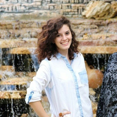 A young woman smiles as she poses for a photograph in front of a fountain.