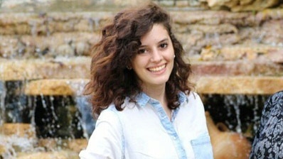 A young woman smiles as she poses for a photograph in front of a fountain.