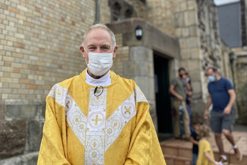 A priest wears a mask outside church