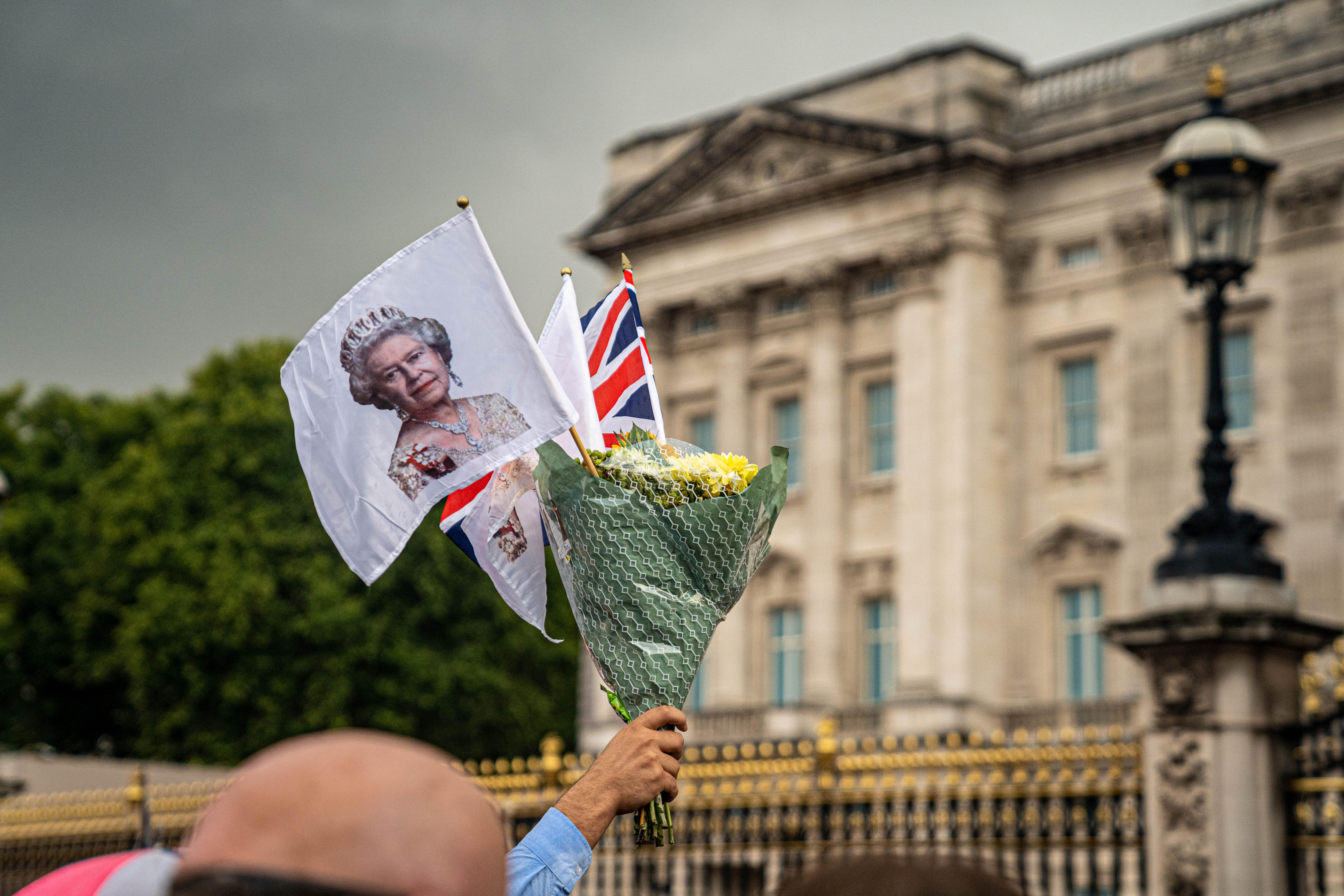 A hand holds up a bunch of flowers with a small union jack and flag bearing the Queen's face
