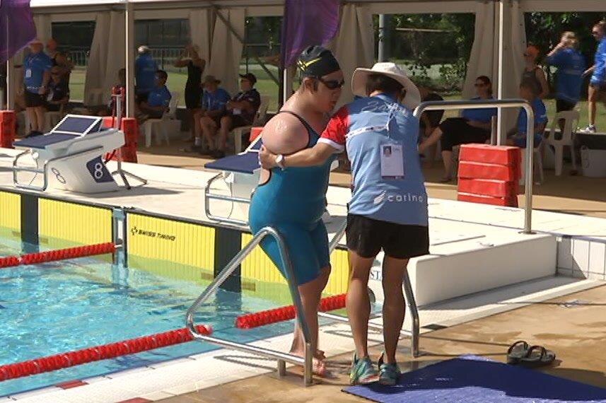 A coach helps a swimmer without arms into the pool.