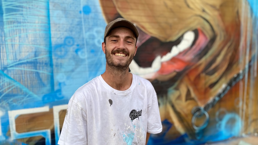a young man smiling in front of street art